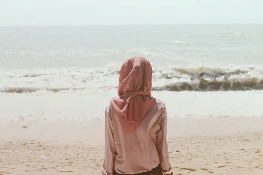 Profile image of a girl with a hijab sitting from behind on the beach facing the sea