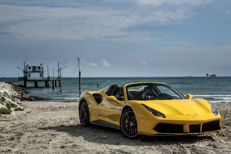 Photo of a well-made yellow Ferrari 488 Spider on the beach
