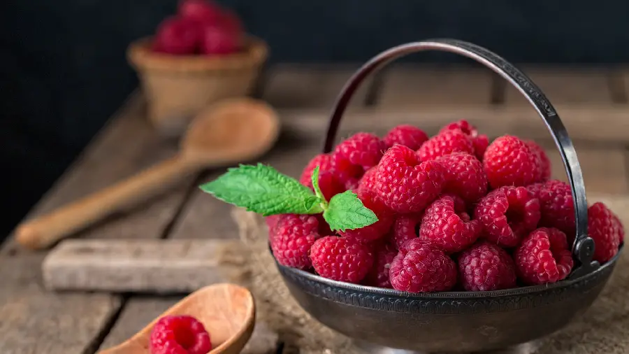 Stock photo of red raspberries in a metal container with wooden spoons