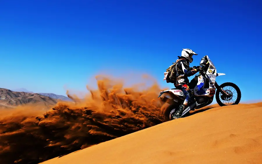 Interesting and spectacular image of a Dakar Rally motorcycle rider getting crushed in a desert full of sand