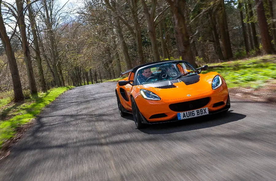 Photo of a fast and light orange Lotus car on a lush forest road