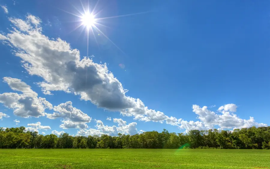 A highlight photo of a green field, a blue sky, and a bright sun