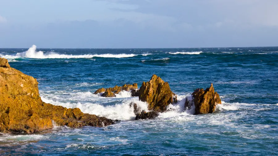 A background of the endless ocean and blue waves crashing against the rocks