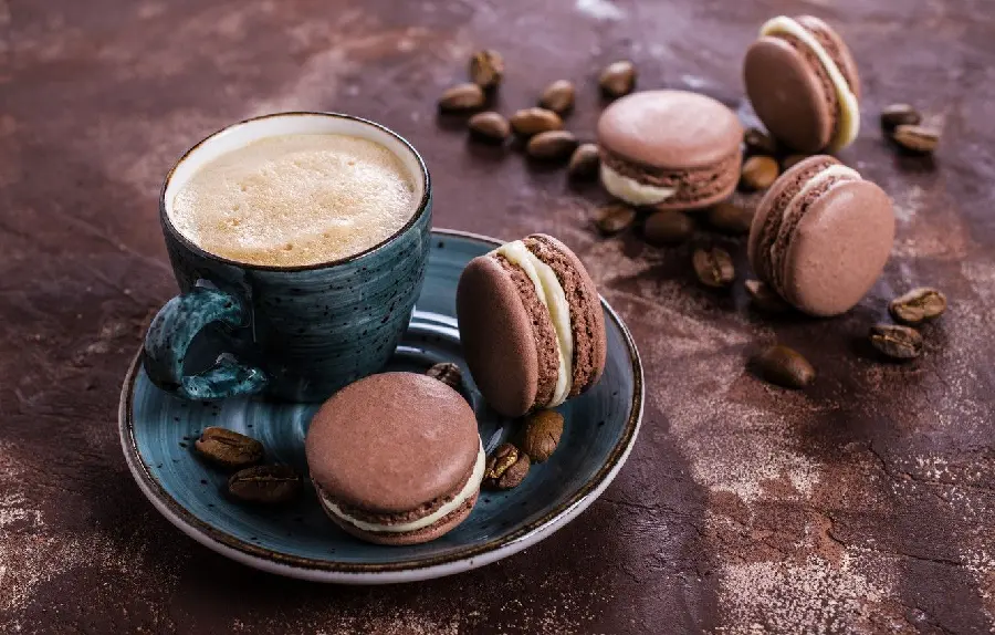 A delicious coffee photo with a beautiful chocolate macaron next to it 