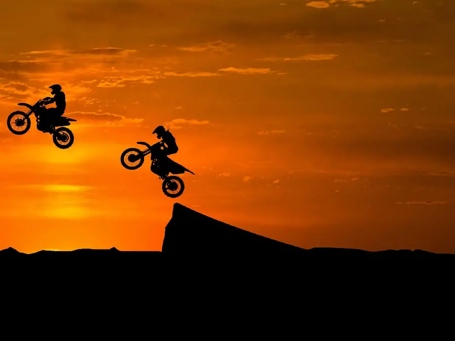 Wallpaper of high jumps with motocross on a desert track in a calm sunset