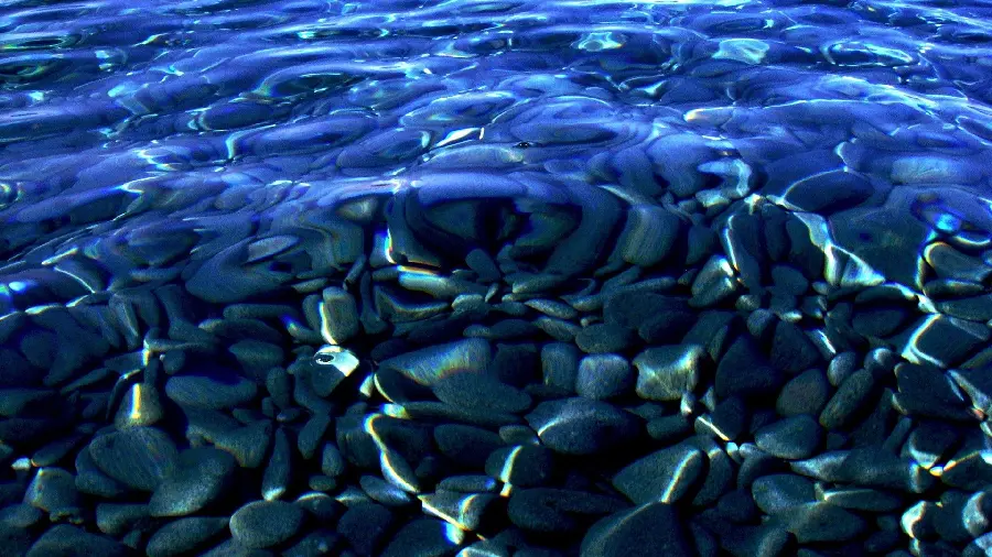 Stock photo of cool water of a clear lake with black stones on the bottom of the water