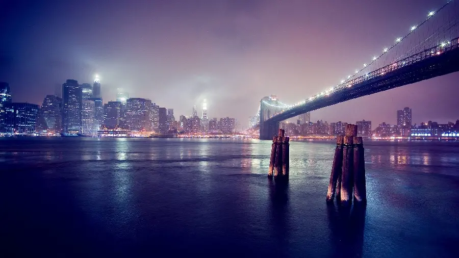 Wallpaper of suspension bridge in a city with tall skyscrapers under pink night smog