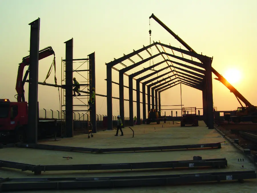 Background photo of large steel building under construction at sunset