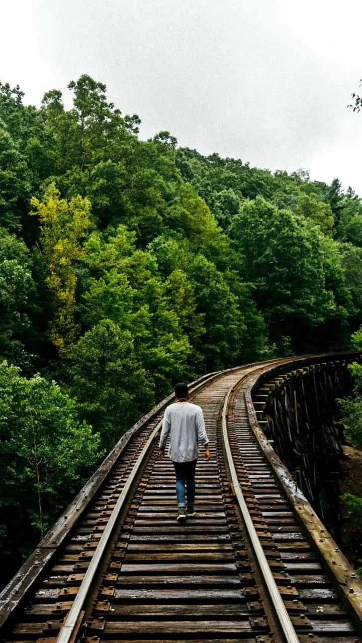 Photo of a lonely man running on the railroad tracks next to the trees 