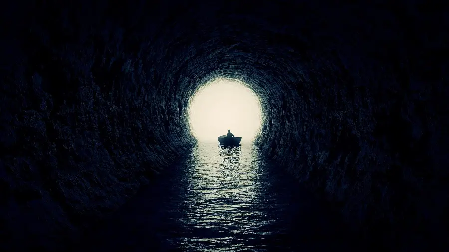 A picture of a man riding a small boat at the mouth of a dark cave in the sea 