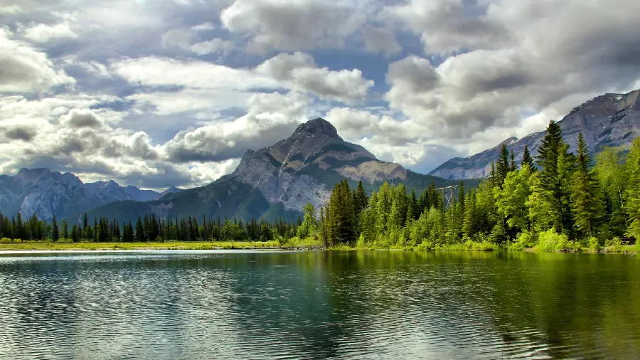 The most beautiful image of a vast and deep lake with mountains and green trees and a cloudy sky 