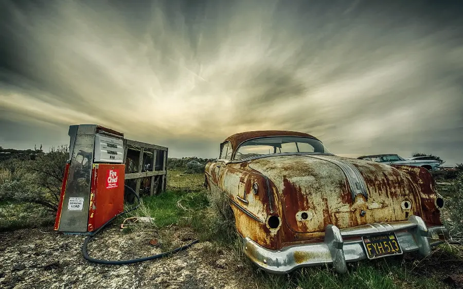 Wallpaper of a worn out car next to an old gas station