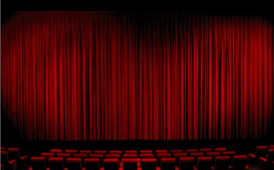 Photo of a cinema screen in a hall arranged with red chairs 