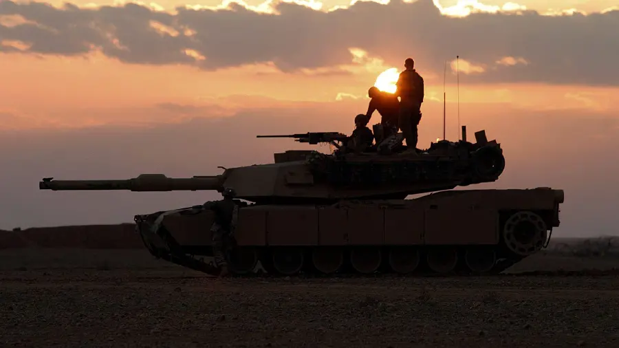 Image of soldiers riding a tank with a sunset background 