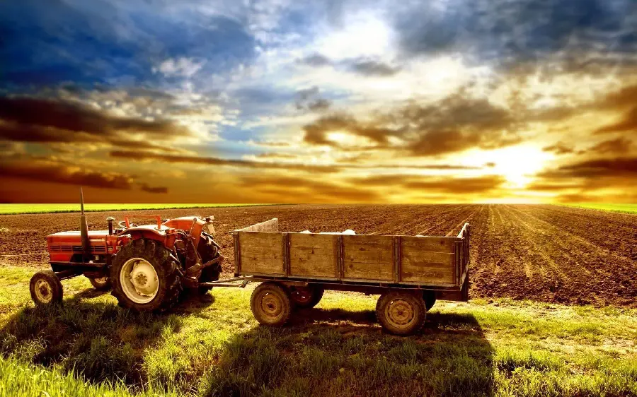 Photo of a tractor in a farm field with direct sunlight and facing the sunset