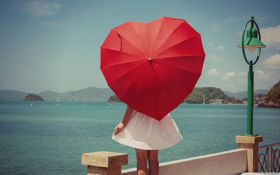 Photo of a red umbrella in the shape of a heart in a girl's hand