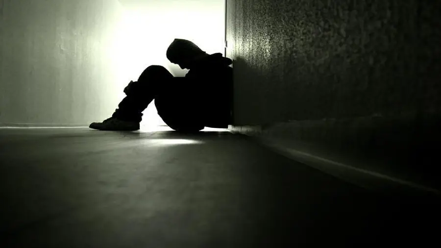 Sad and lonely boy in the corner of the room and kneeling on the side crying and alone