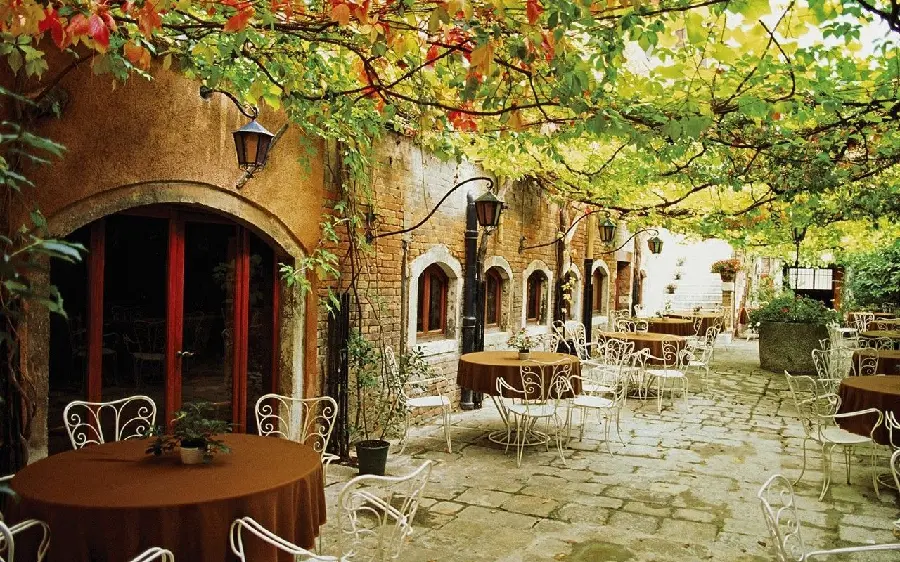 Image of tables and chairs of cafes in Italy in the middle of the street and under the shade of trees