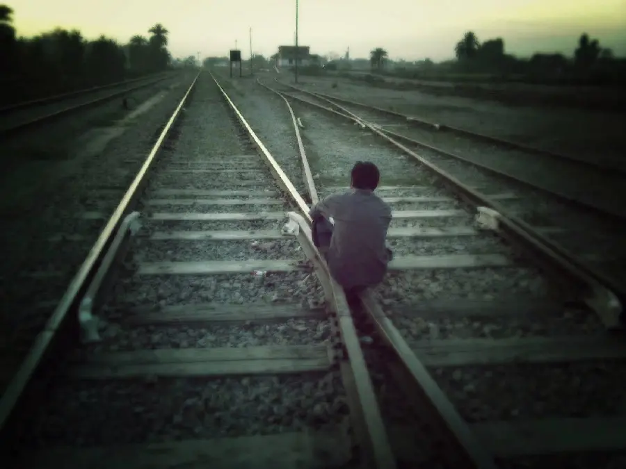 High quality image of a lonely boy sitting on the train tracks, kneeling on his lap